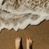 imagem de pés na areia com a água do mar quase a alcançá-los
