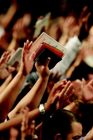 imagem de varias mãos elevadas em clamor, em que uma pessoa está com uma Bíblia nas mãos